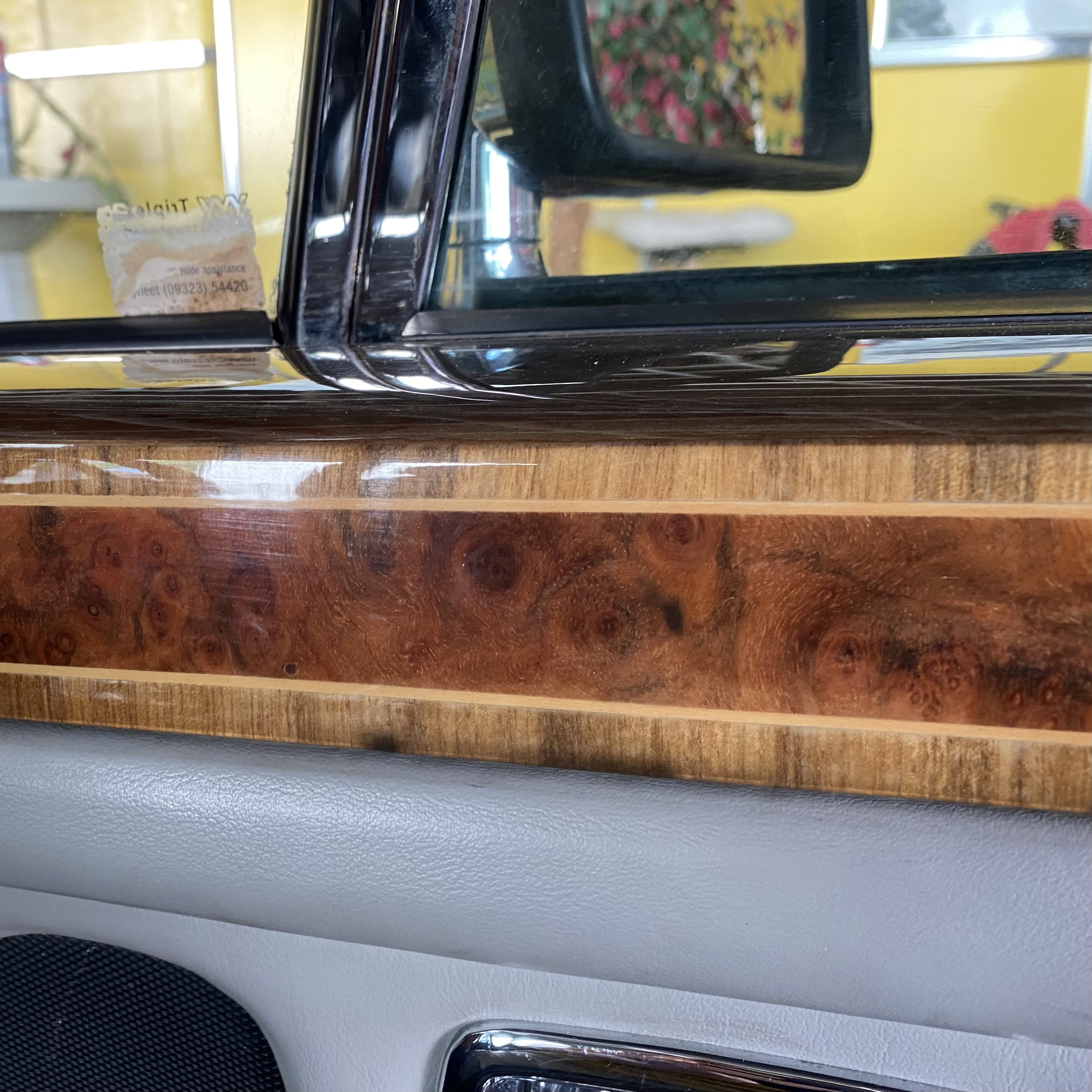 Close-up view of a car door panel featuring decorative wood trim with a polished finish and soft leather texture.