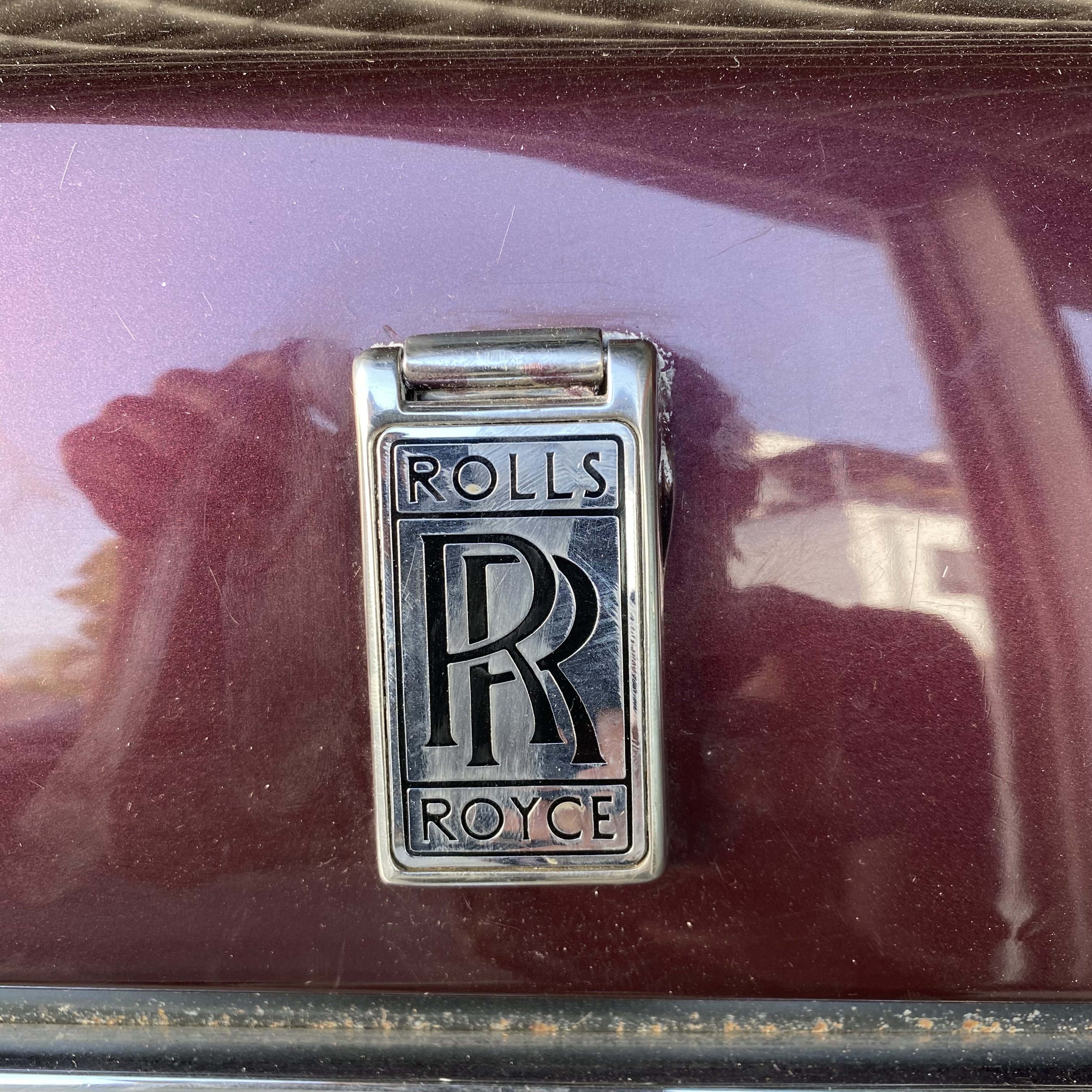 Close-up of a Rolls Royce emblem on a maroon car surface.