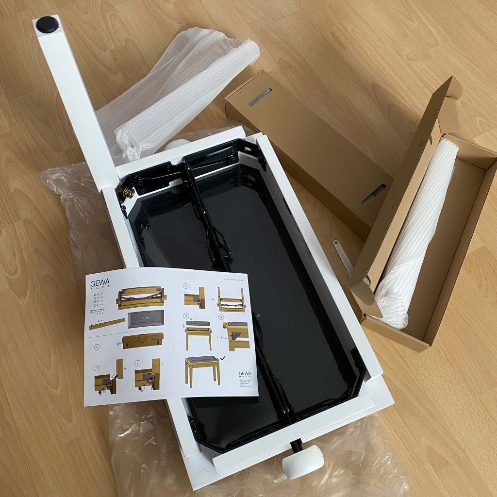 An assembly view of a desk, with a white tabletop, a black drawer section, packaging materials, and an instruction manual showing assembly steps.