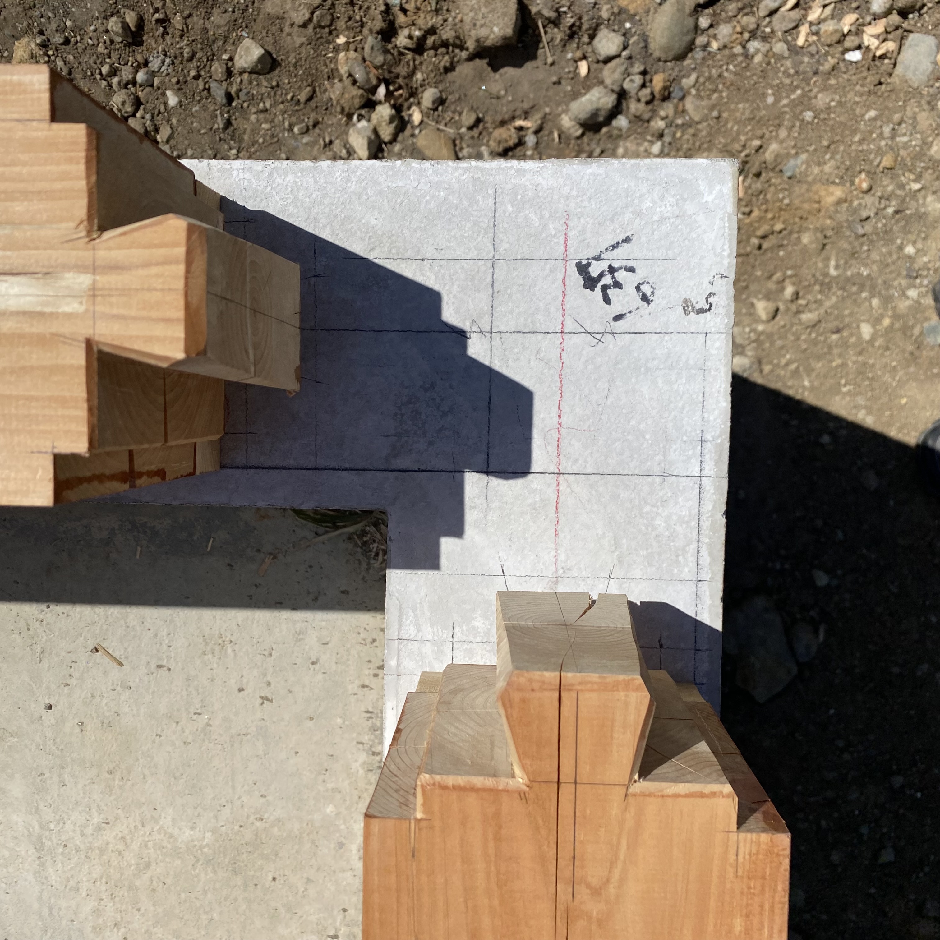 Top view of wooden beams positioned over a concrete base with marked lines and measurements for construction.