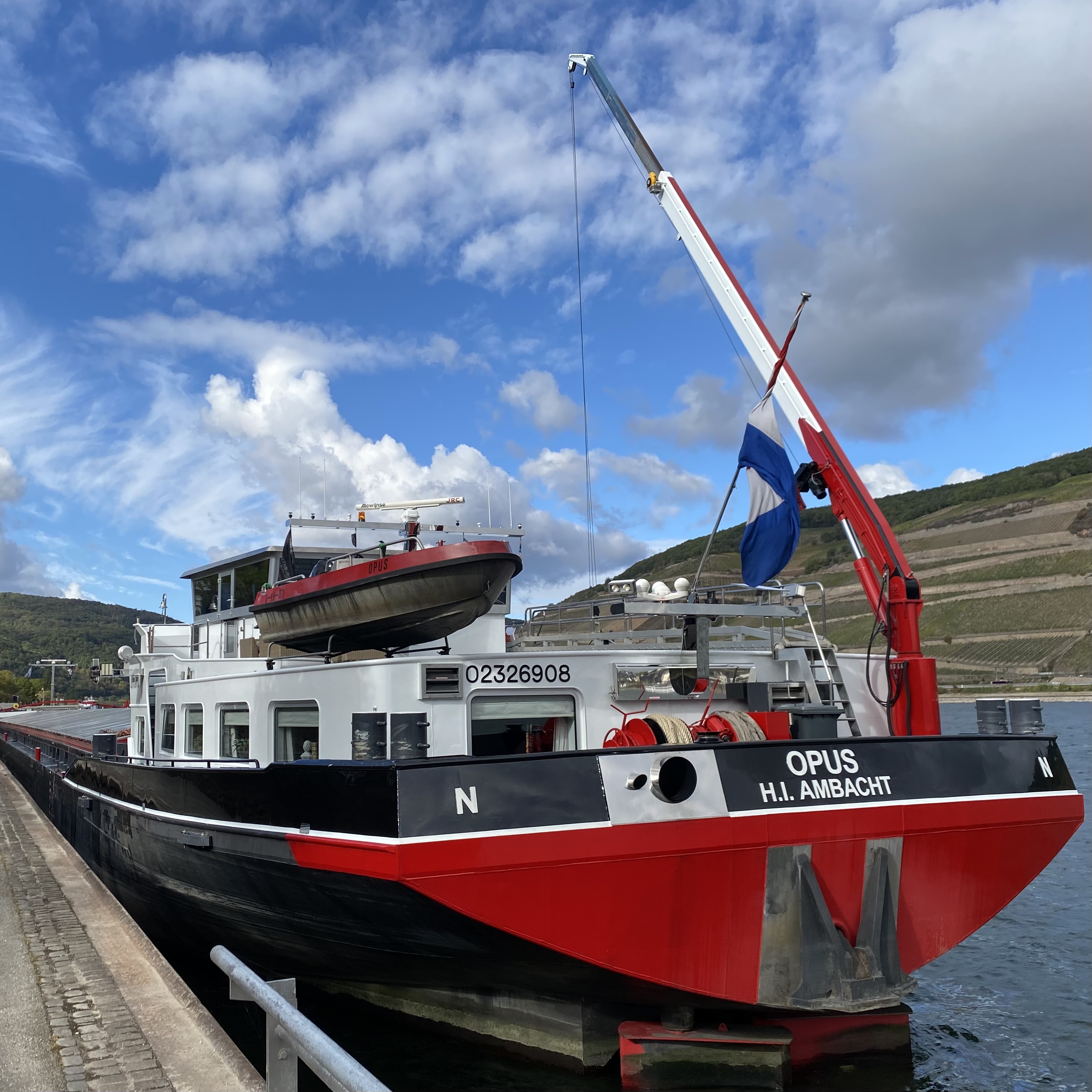 A red and black cargo ship named 'OPUS' docked at a port with a blue sky and white clouds in the background.