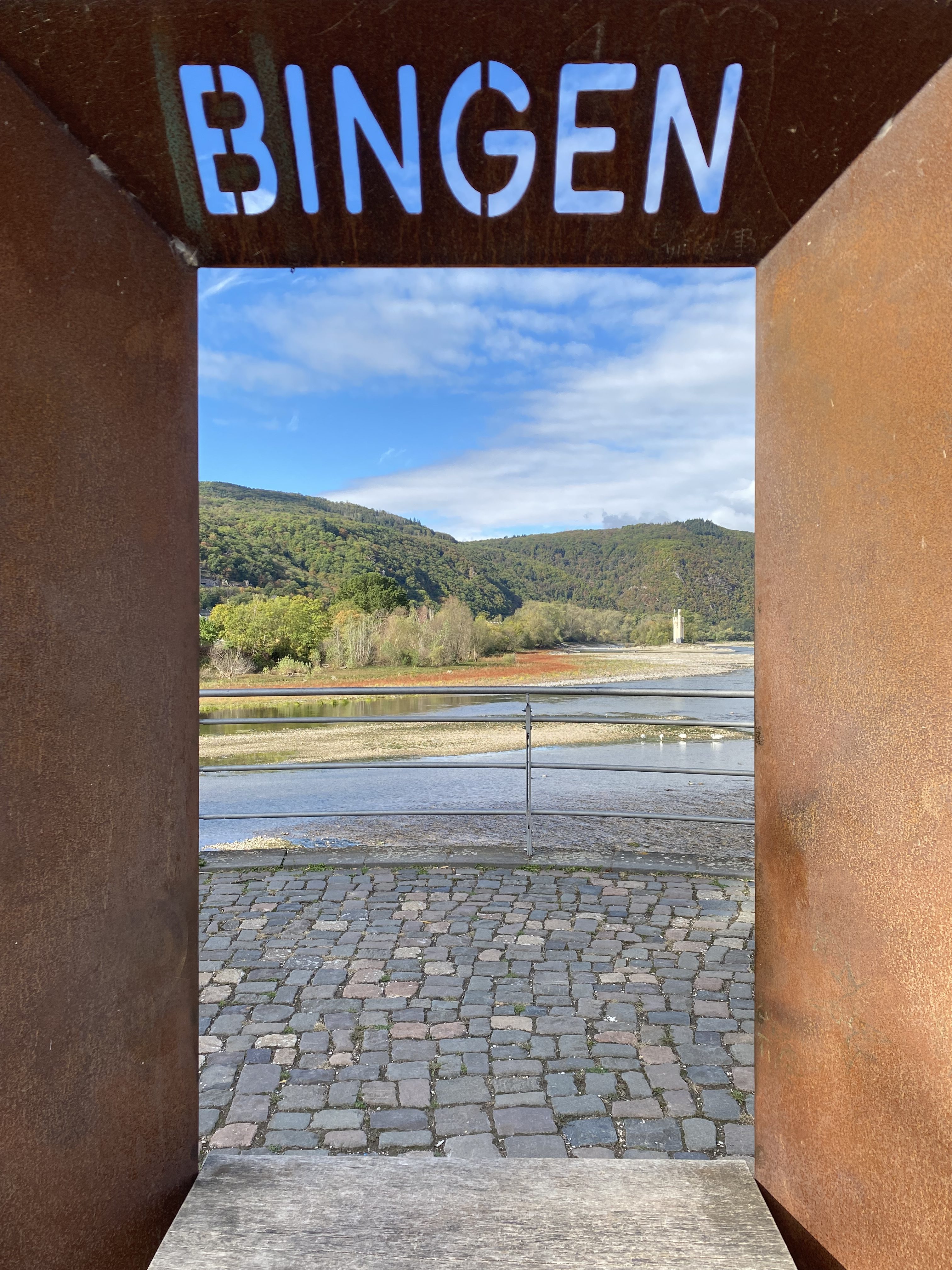 View of the Rhine River and hills framed by a rusted structure with the word 'BINGEN' at the top.